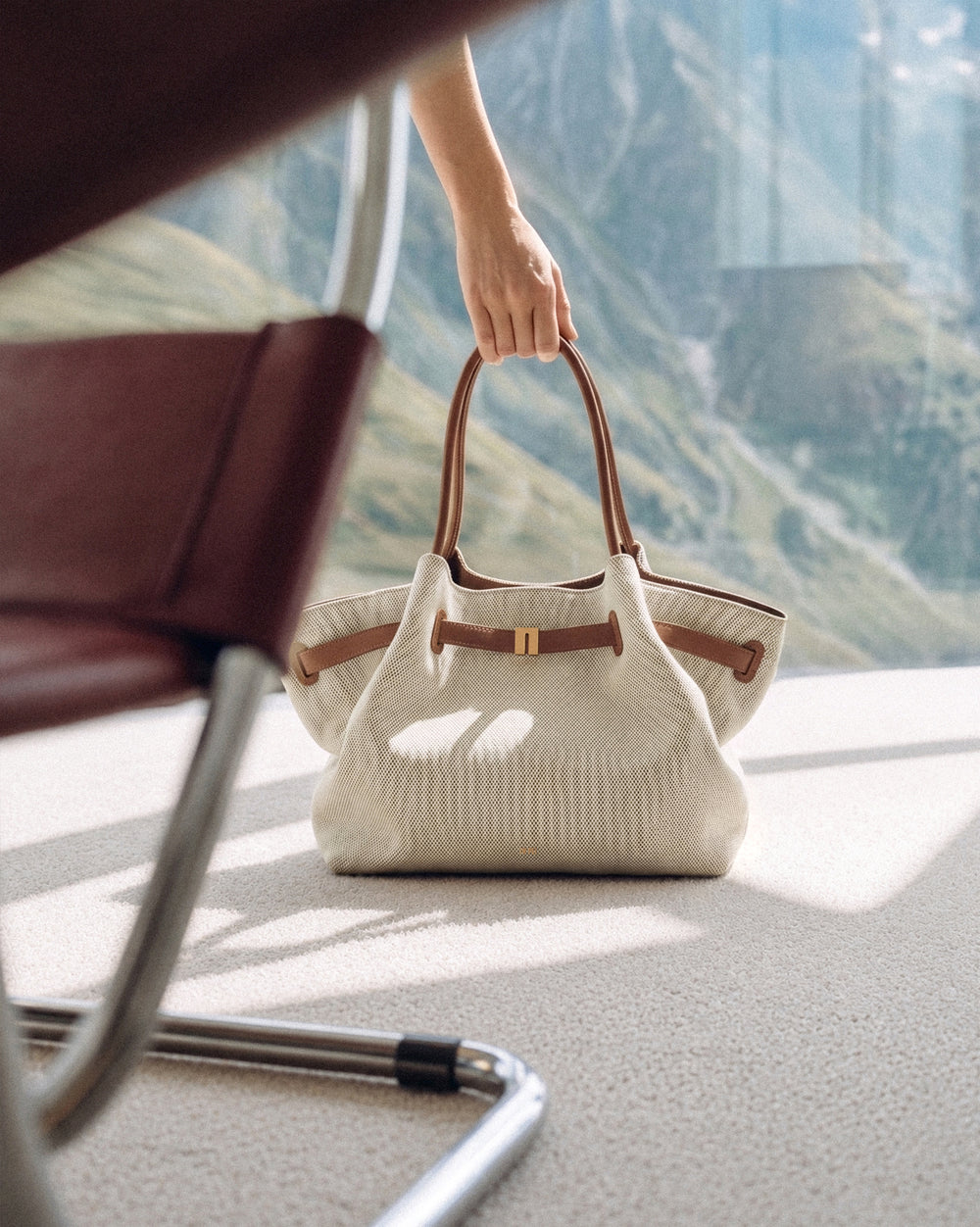 JW PEI cream handbag beside a leather chair overlooking the sea
