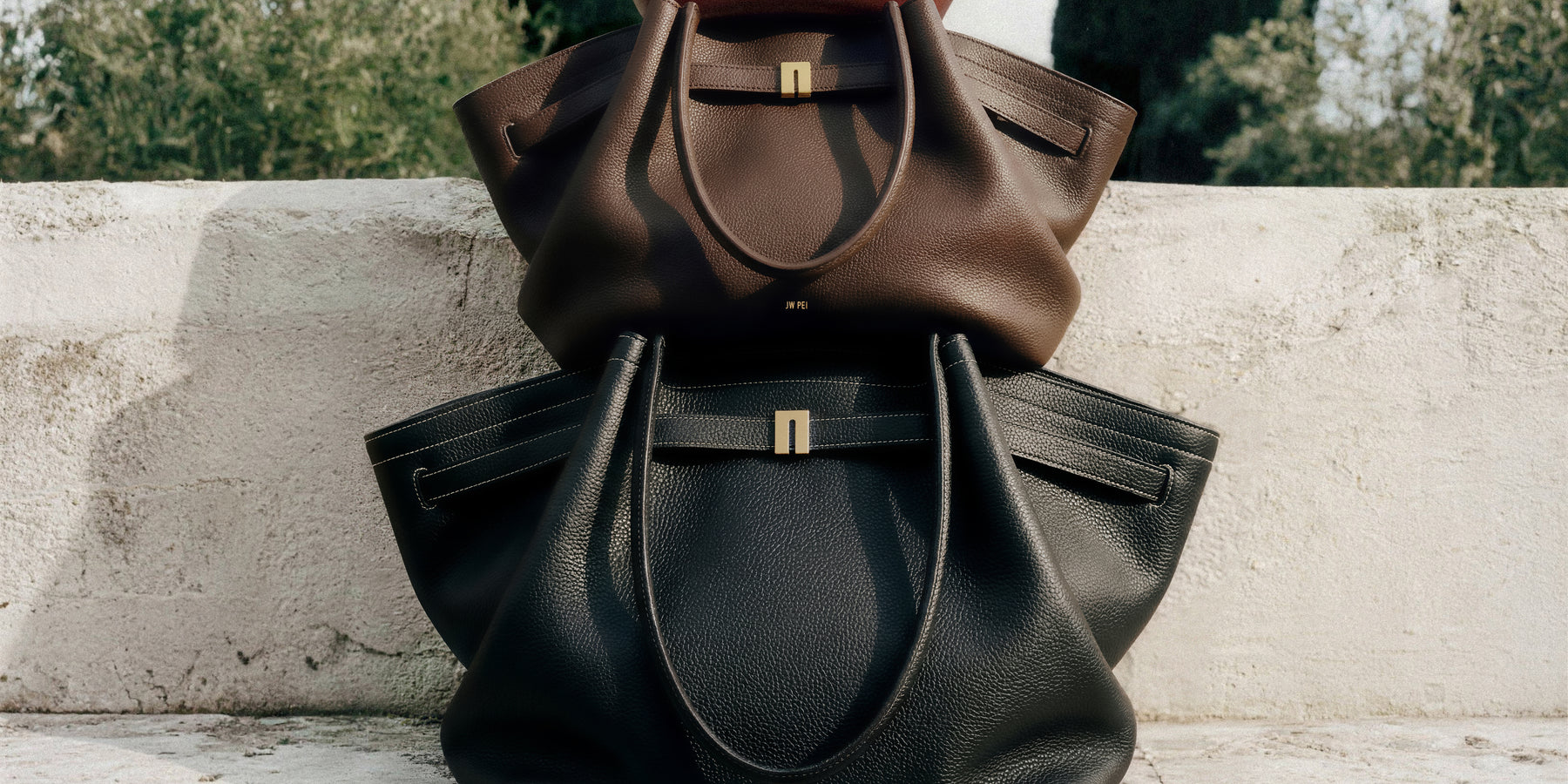 JW PEI handbags in three colours styled on a stone bench